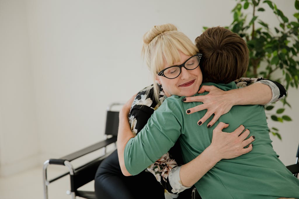 Woman in Black Eyeglasses Hugging Woman in Green Shirt